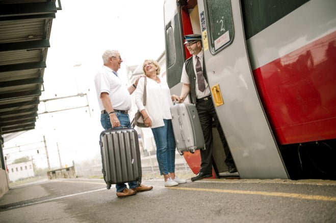 Eldre par med kofferter møter konduktør i tog døren. foto